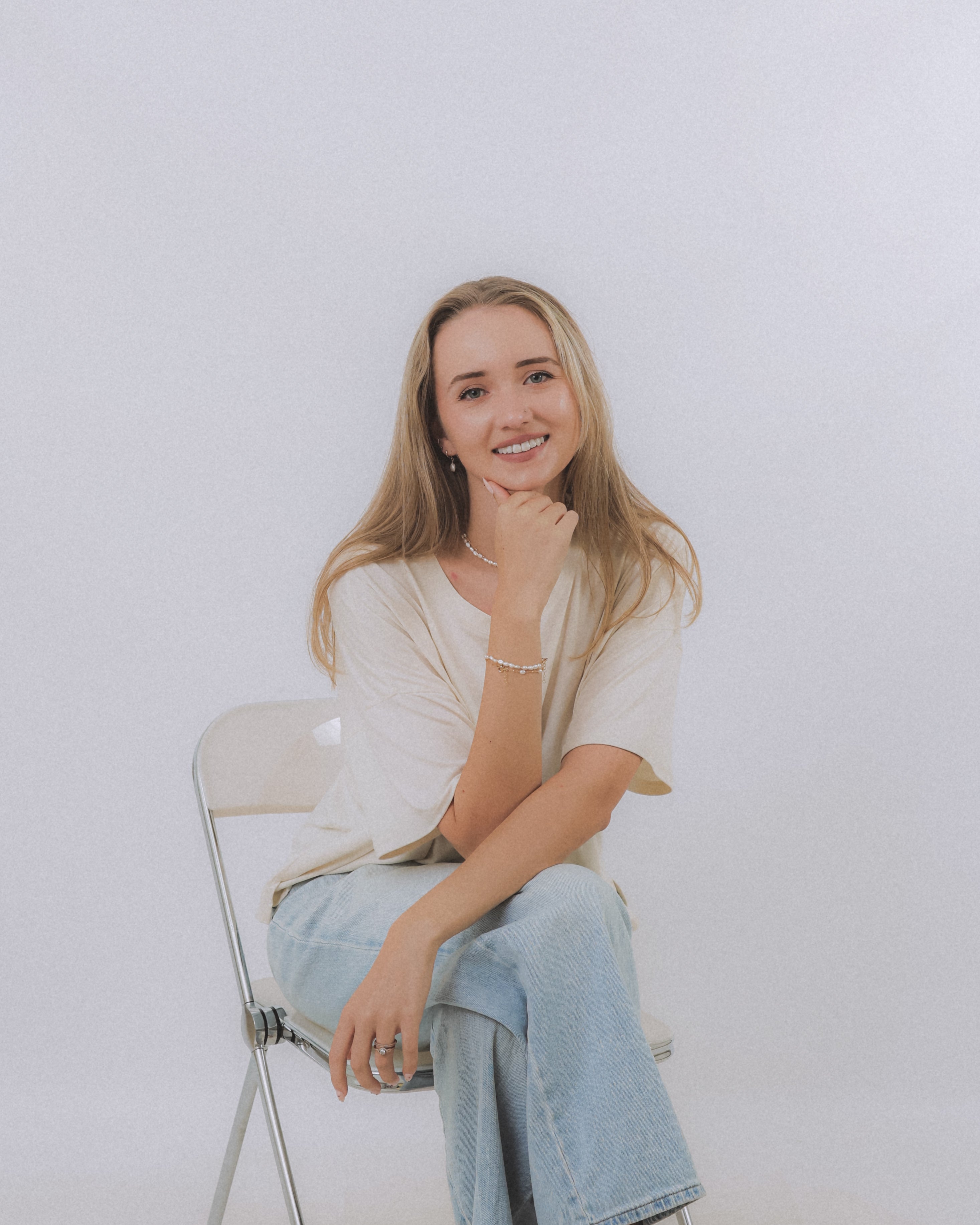 founder of sand + salt sitting and smiling with chin resting on hand, wearing gold-filled and pearl jewelry