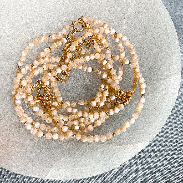 mother of pearl beaded bracelets sitting in quartz dish; gold-filled and gemstone jewelry sand + salt